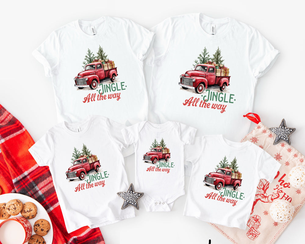 White t-shirts with red truck graphics and 'Jingle All the Way' text, surrounded by Christmas-themed items.