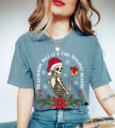 A woman sitting and wearing a blue t-shirt with a skeleton character and the text 'DEAD INSIDE BUT IT'S THE HOLIDAY SEASON' on it.