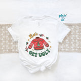 A white Christmas themed t-shirt with text and decorations, placed on a white surface with a red ugly sweater and the text " Let's get Ugly"