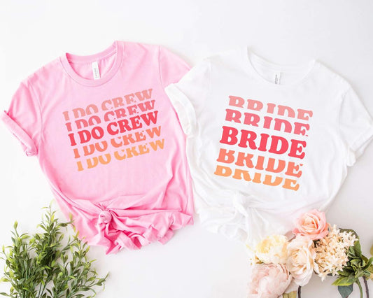 Two crew neck t-shirts, one pink and one white, with bold lettering. The pink one reads 'I DO CREW' and the white one reads 'BRIDE'.