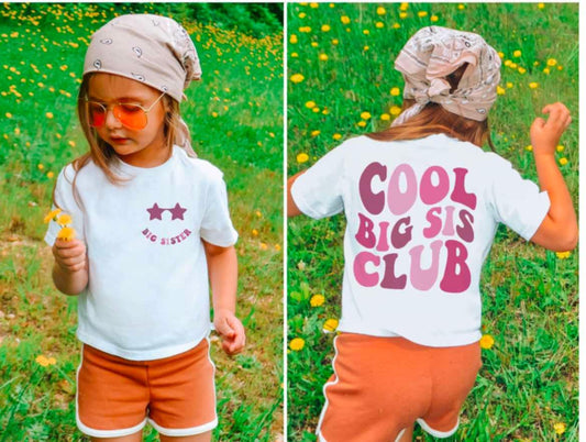 A child wearing a white t-shirt with the text 'COOL BIG SISTER CLUB' printed in pink, paired with orange shorts, is seen in two different poses in a grassy field with flowers around.