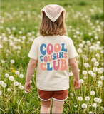 Child in a field of dandelions wearing a 'Cool Cousins Club' t-shirt.