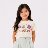 Young girl wearing a 'big sister' t-shirt with colorful text on a white background