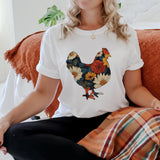Person wearing a white t-shirt with a colorful rooster design sitting on a couch.