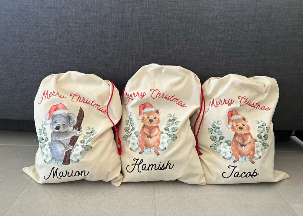 Three personalized Christmas sacks with animal illustrations and names on a gray surface.