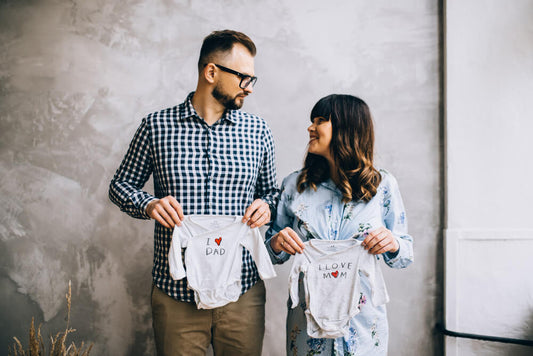 Pregnancy announcement phot of parents holding onsies