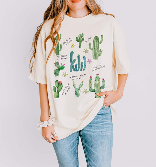 A woman wearing a white crew neck t-shirt with a graphic of various cactus plants on it, paired with blue jeans.