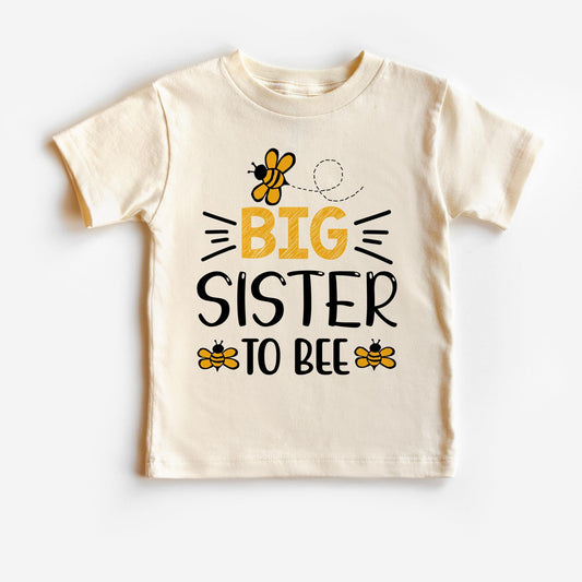 A white t-shirt with 'Big Sister to Bee' text and a bee graphic design.