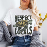 A person wearing a white t-shirt with a green turtle graphic and the text 'RESPECT THE LOCALS' on it.