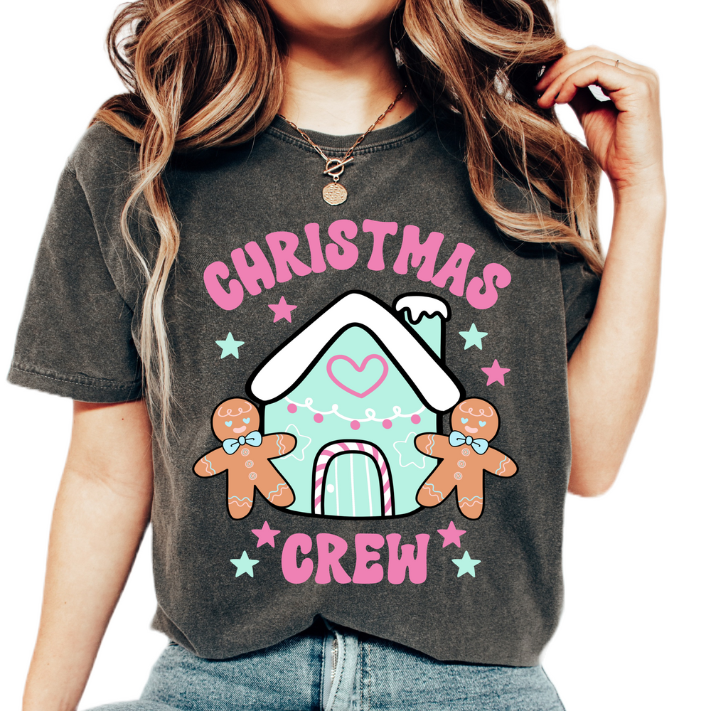 A woman wearing a Christmas Crew t-shirt with a colorful Christmas-themed graphic design, including a gingerbread man, a snowman, and festive decorations.