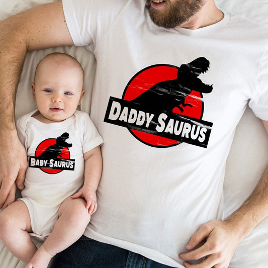 Man and baby wearing matching 'Daddy Saurus' and 'Baby Saurus' shirts.