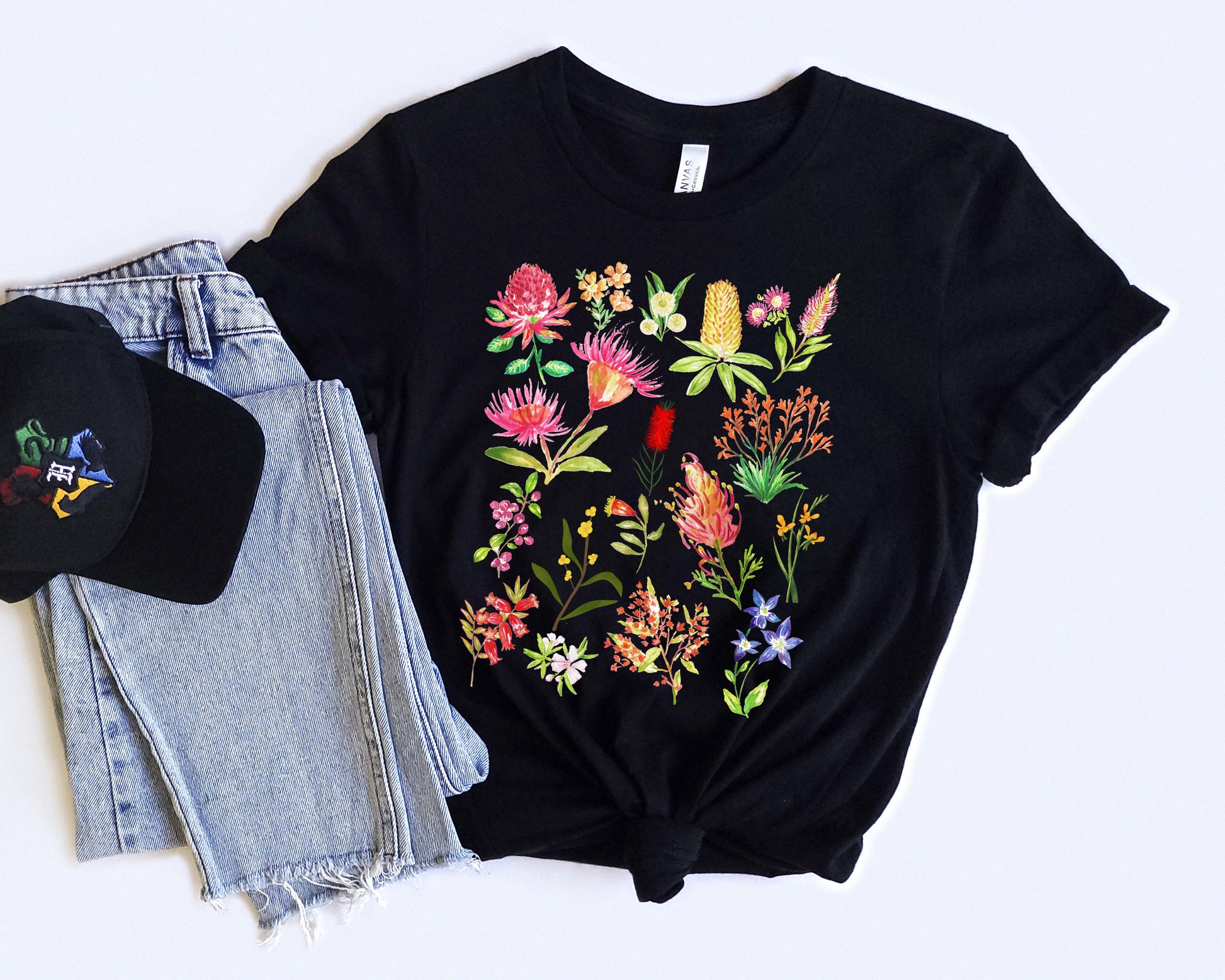 Black t-shirt with colorful Australian floral design, black cap, and denim shorts on a white background