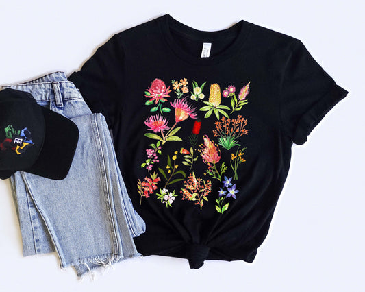 Black t-shirt with colorful Australian floral design, black cap, and denim shorts on a white background