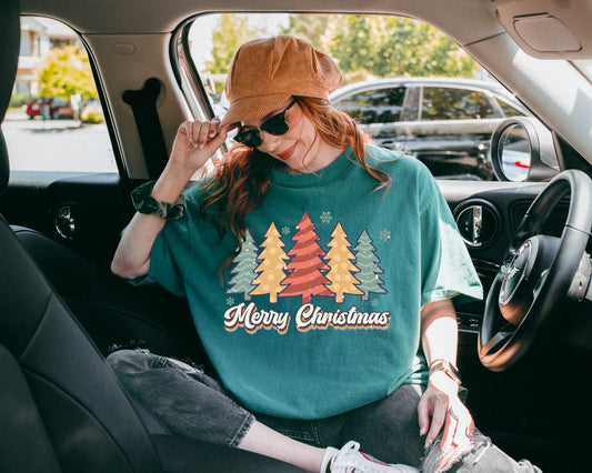 Person sitting in a car wearing an oversized green spruce 'Merry Christmas' sweater with colorful trees. 
