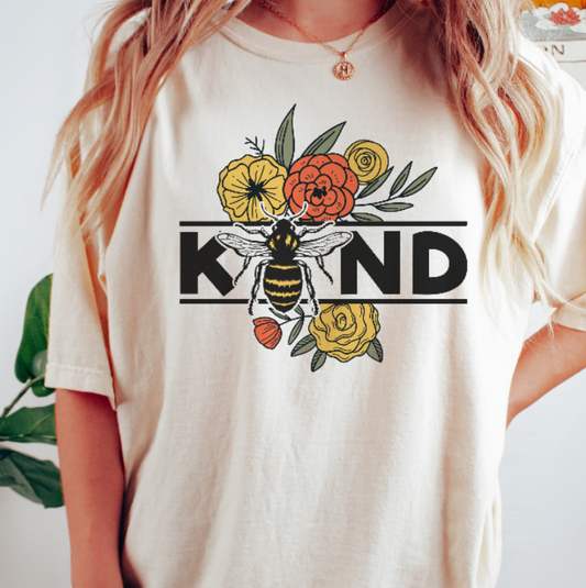 Person wearing an Ivory t-shirt with a bee and floral design and the text 'KIND'.