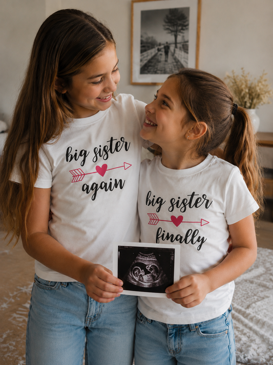 Two sisters wearing 'big sister again' and 'big sister finally' shirts, holding an ultrasound photo.