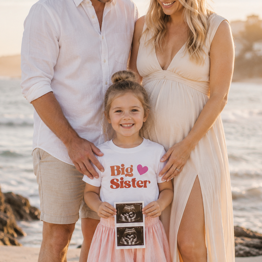 Family of three on a beach with a pregnant woman and a young girl holding an ultrasound photo.