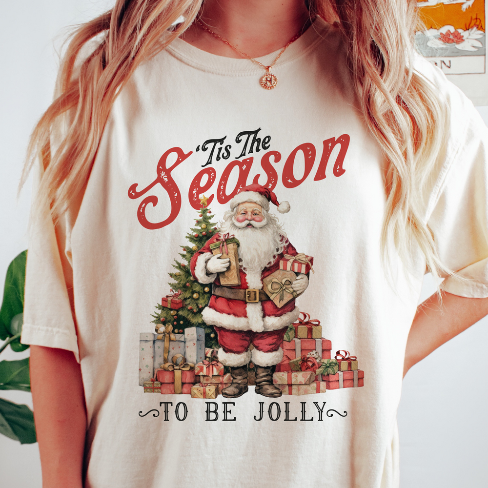 A vintage style Christmas themed t-shirt with Santa Claus and a Christmas tree graphic, and the text '*It's the Season to be Jolly*' on a light background.
