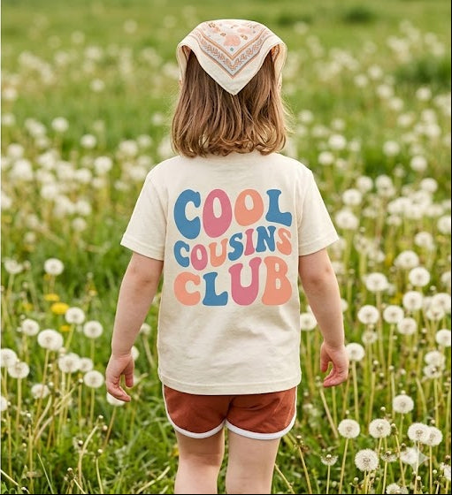 Child in a field of dandelions wearing a 'Cool Cousins Club' t-shirt.