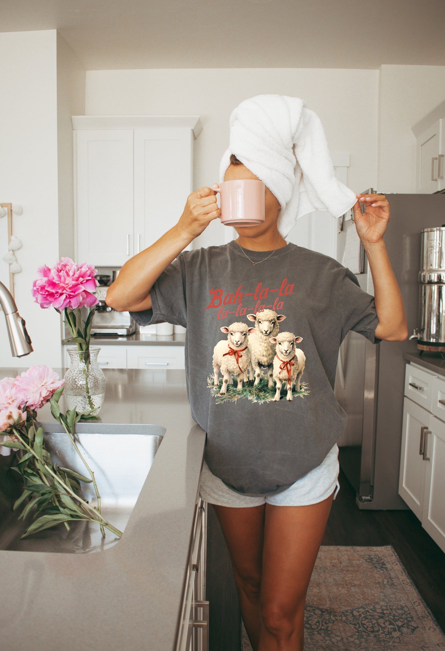 Person in a kitchen wearing a t-shirt with sheep graphics and text.