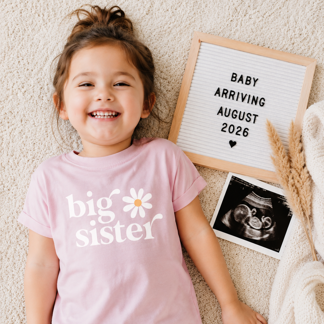 Child wearing a 'big sister' shirt with a letterboard and ultrasound photo in the background.