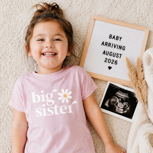 Child wearing a 'big sister' shirt with a letterboard and ultrasound photo in the background.
