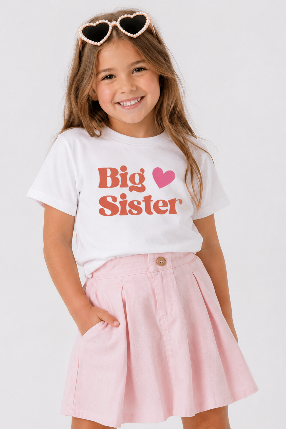 Child wearing a 'Big Sister' t-shirt with a pink skirt on a white background