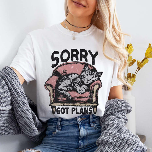 A person wearing a white T-shirt with a graphic print of a cat and the text 'Sorry Got Plans'.