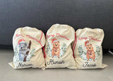 Three personalized Christmas sacks with animal illustrations and names on a gray surface.