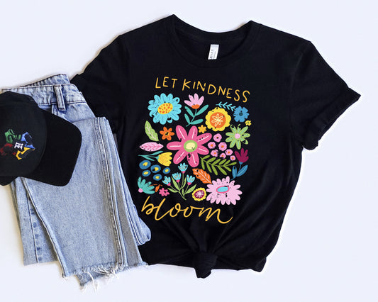 Black t-shirt with colorful floral design and 'Let Kindness Bloom' text, paired with a black cap and jeans on a white background.
