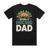Black t-shirt with 'Kinda Busy Being a Hiking Dad' text and mountain graphic on a white background