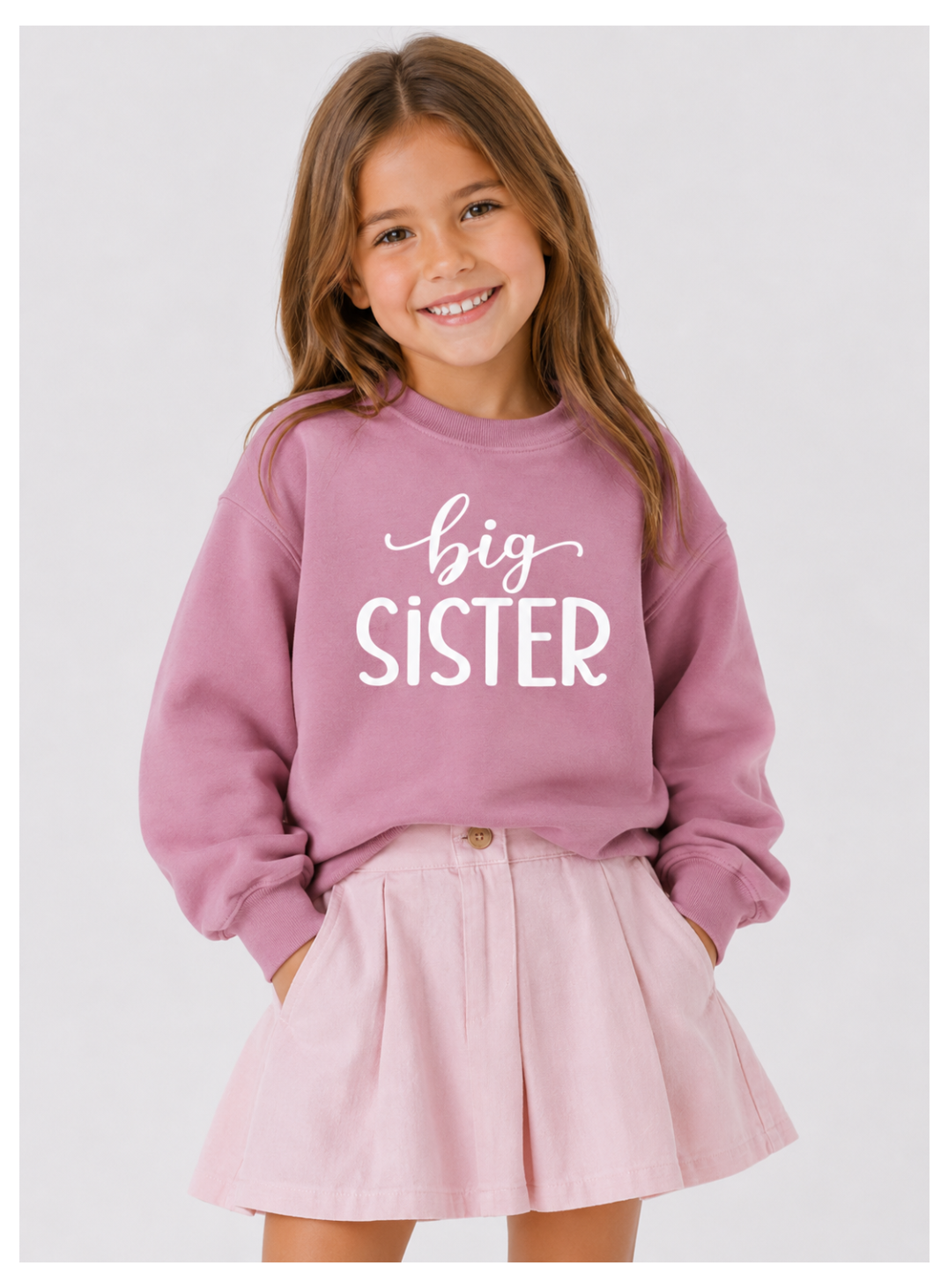 Young girl wearing a pink 'big sister' sweatshirt and pink skirt on a white background