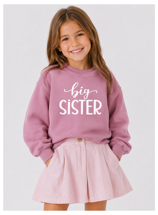 Young girl wearing a pink 'big sister' sweatshirt and pink skirt on a white background