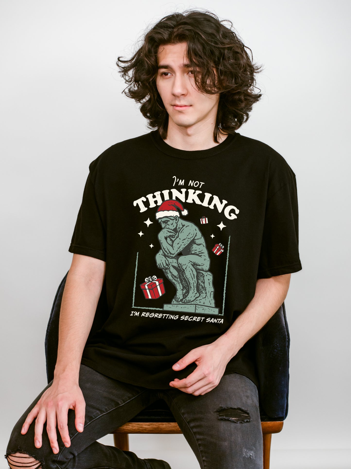 Person wearing a black t-shirt with a Christmas graphic design that says " I'm not thinking, I'm regretting secret santa"
