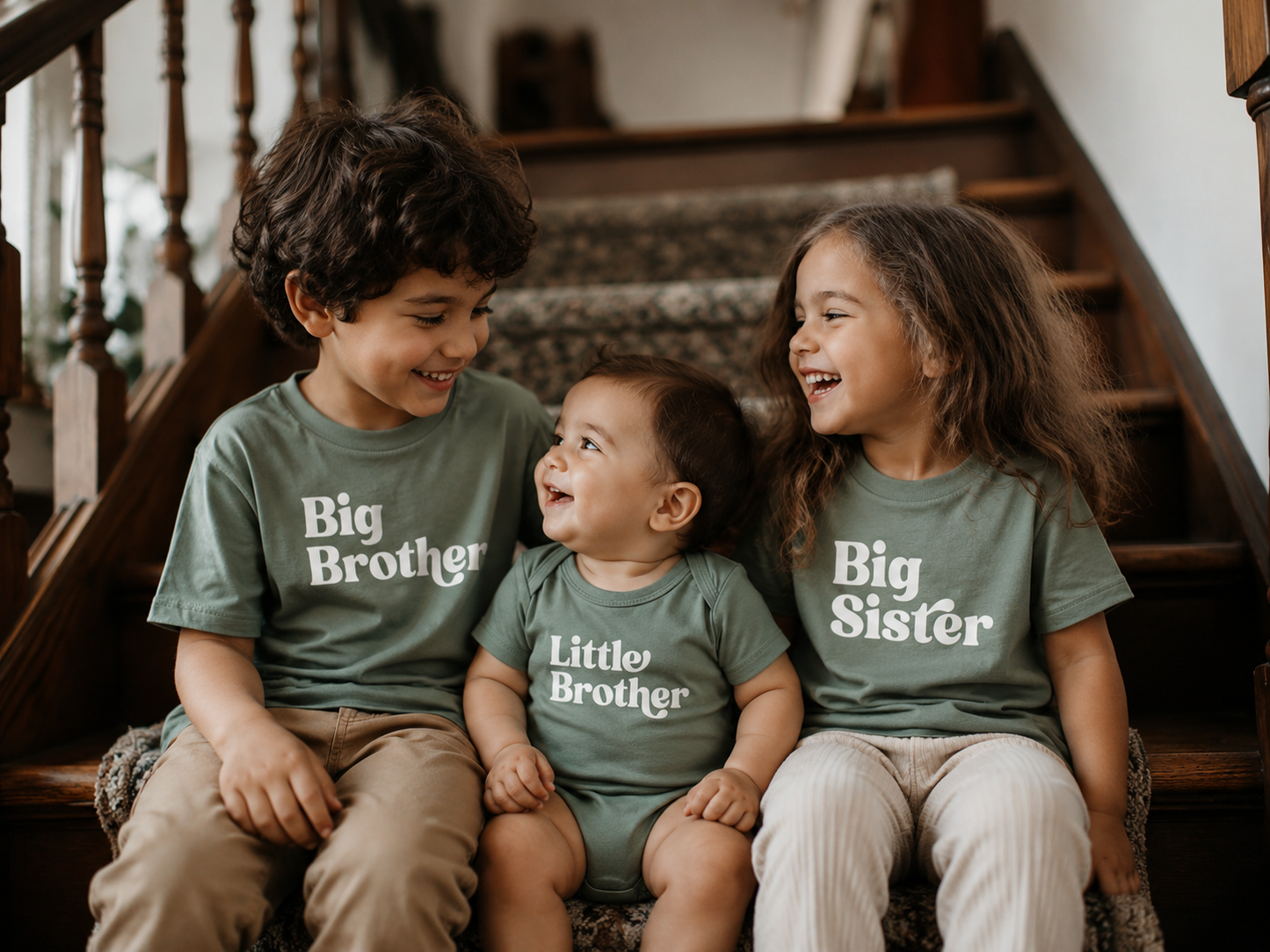 Three children sitting on a staircase wearing matching shirts labeled 'Big Brother', 'Little Brother', and 'Big Sister'.